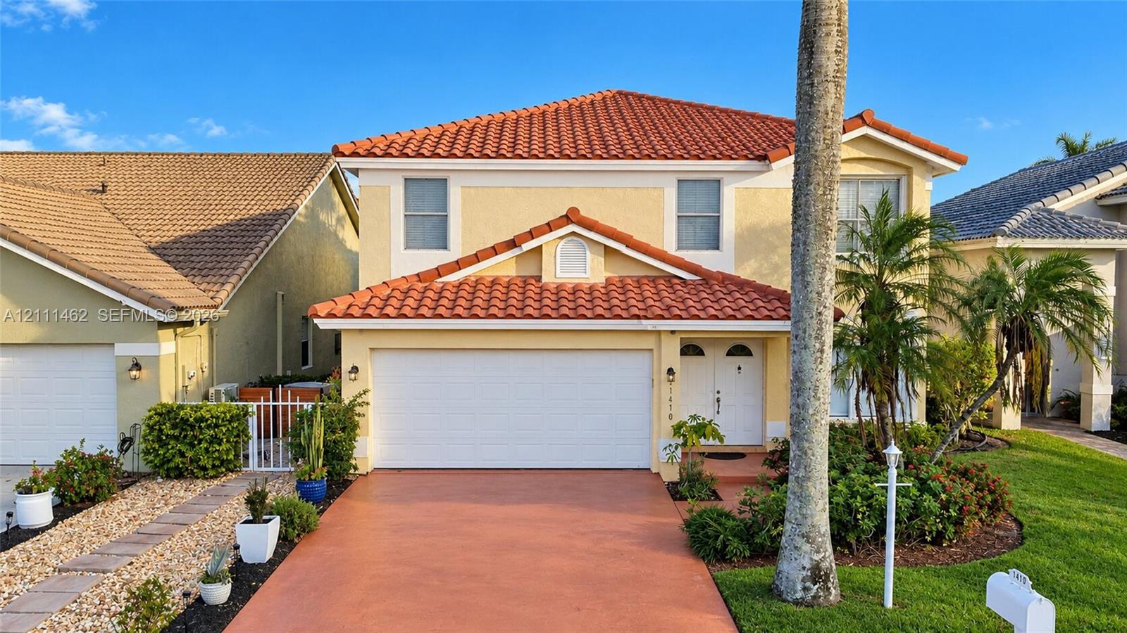 Two-story residence featuring a terracotta-tiled roof, stucco facade, multi-pane windows, and a paved driveway leading to an attached two-car garage Two-story residence featuring a terracotta-tiled roof, stucco facade, multi-pane windows, and a paved driveway leading to an attached two-car garage