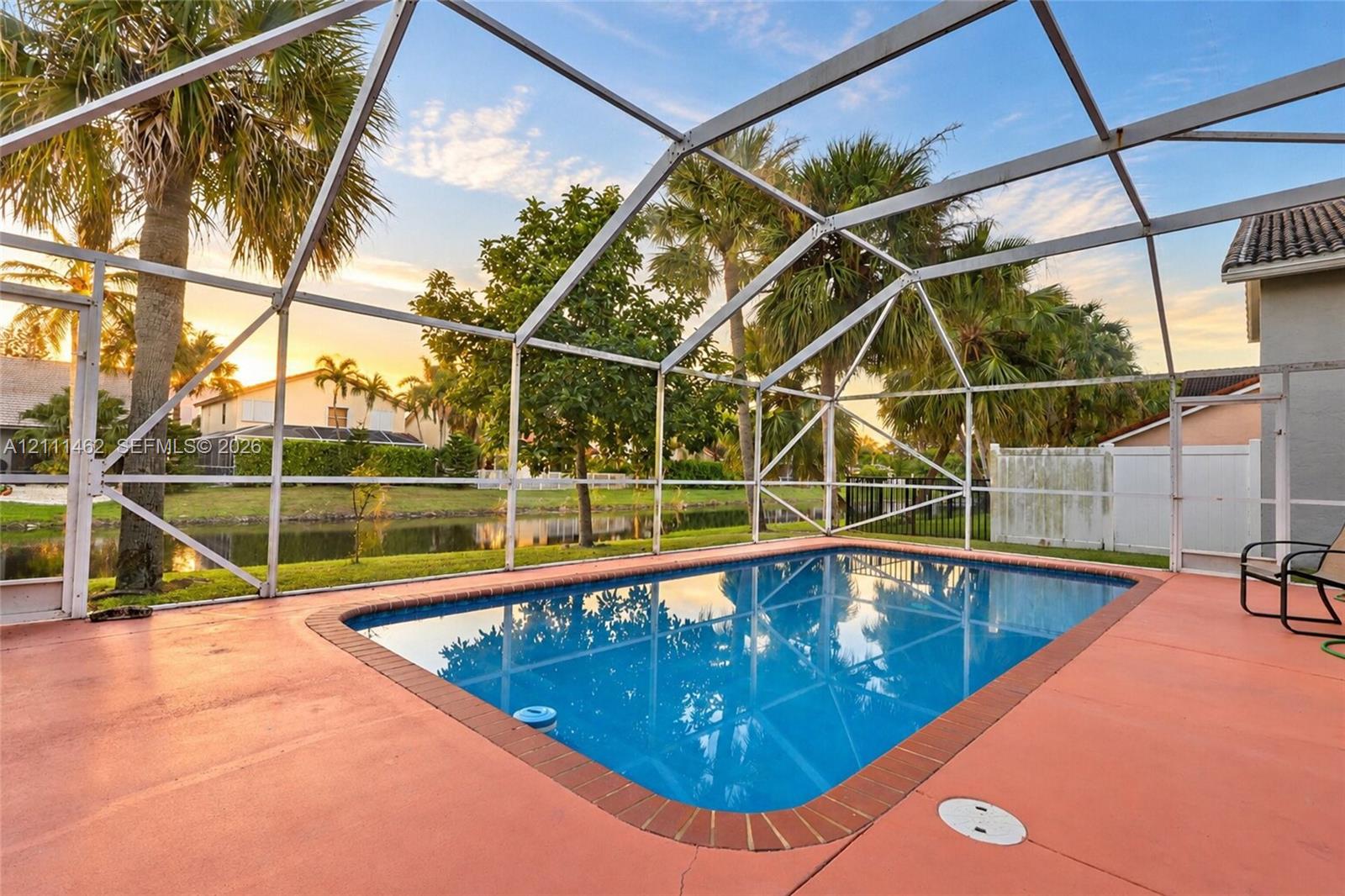 Screen-enclosed swimming pool featuring a brick-tiled perimeter and a concrete patio deck, situated on a waterfront lot with mature palm trees