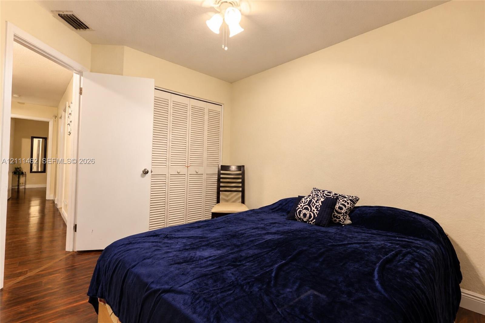 Room featuring wood-finish flooring, ceiling-mounted light fixture, and built-in closet with louvered doors