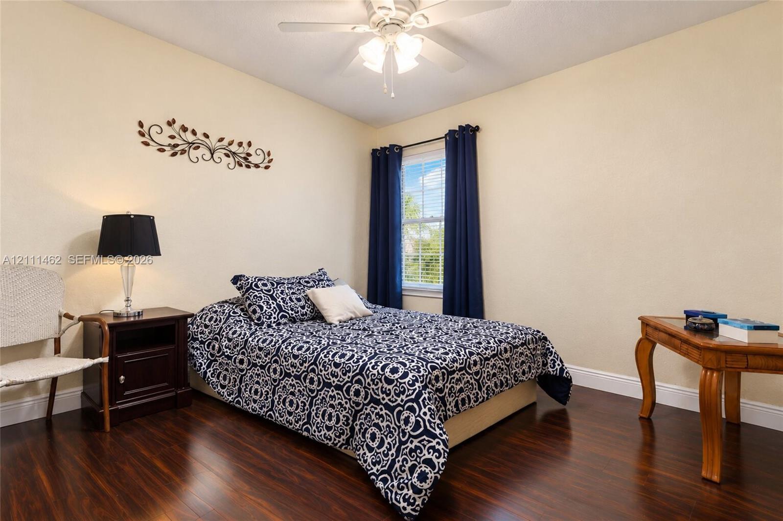 Dark wood-finish flooring, central ceiling fan with integrated lighting, and single window with light-filtering capability