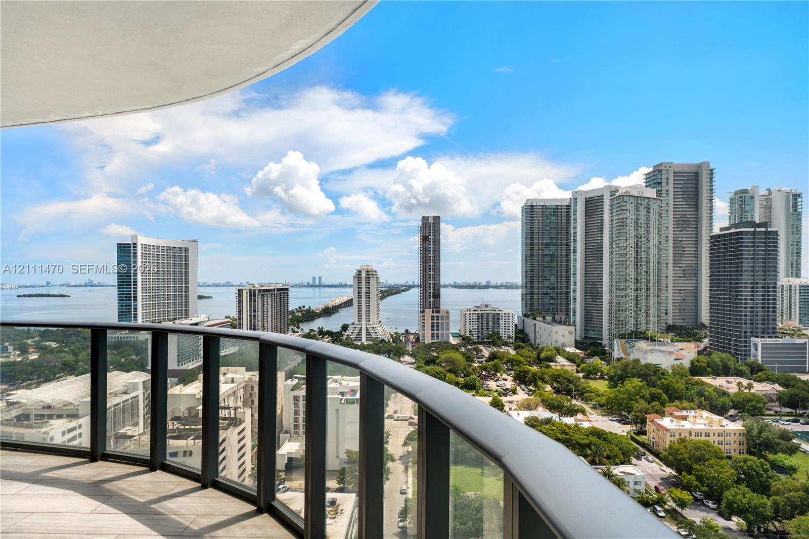 Curved balcony featuring tile flooring and a frameless glass railing with metal trim, showcasing expansive urban and water scenery