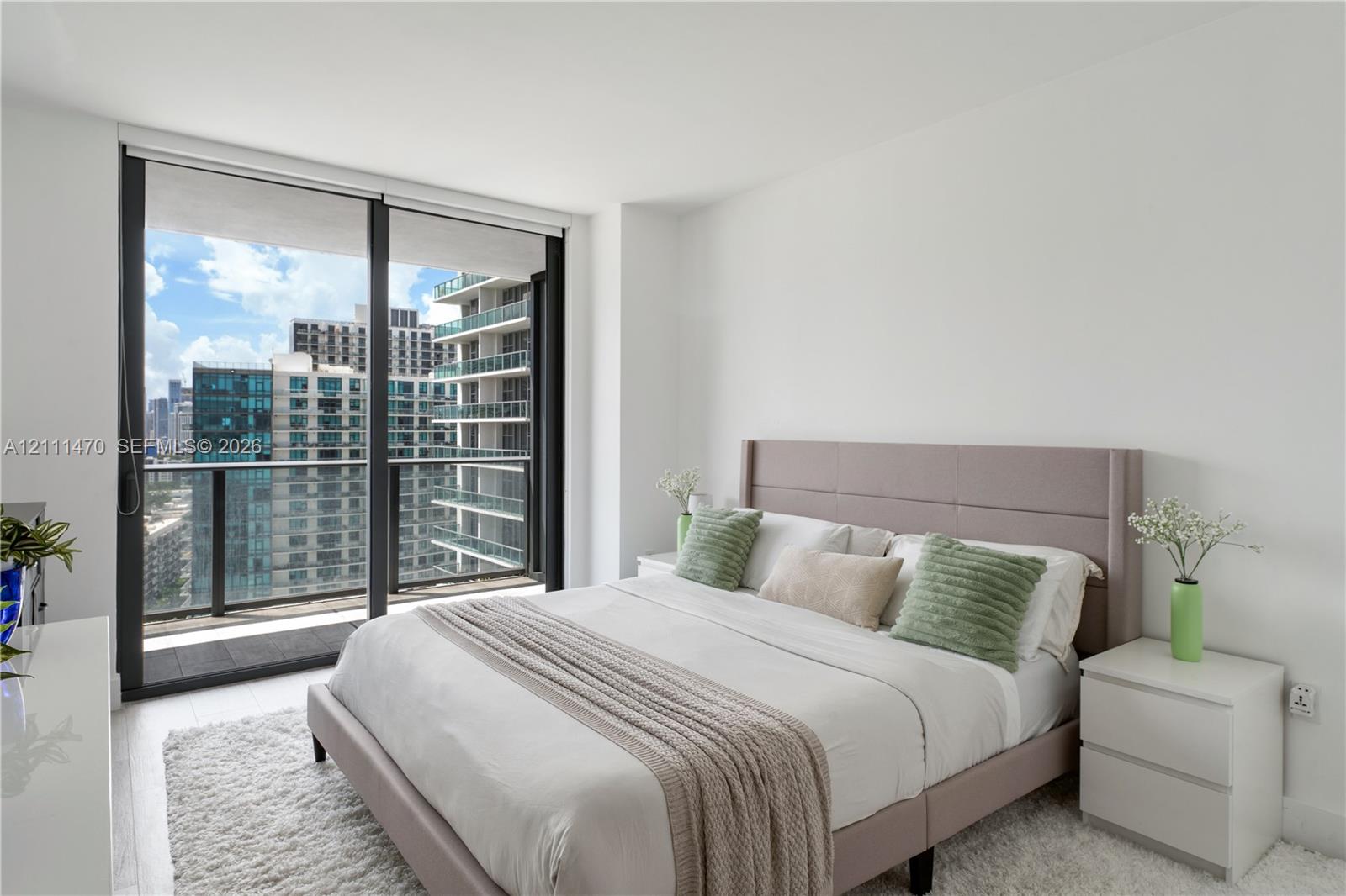 Floor-to-ceiling glass sliding doors, private balcony with metal railing, and neutral wall finishes