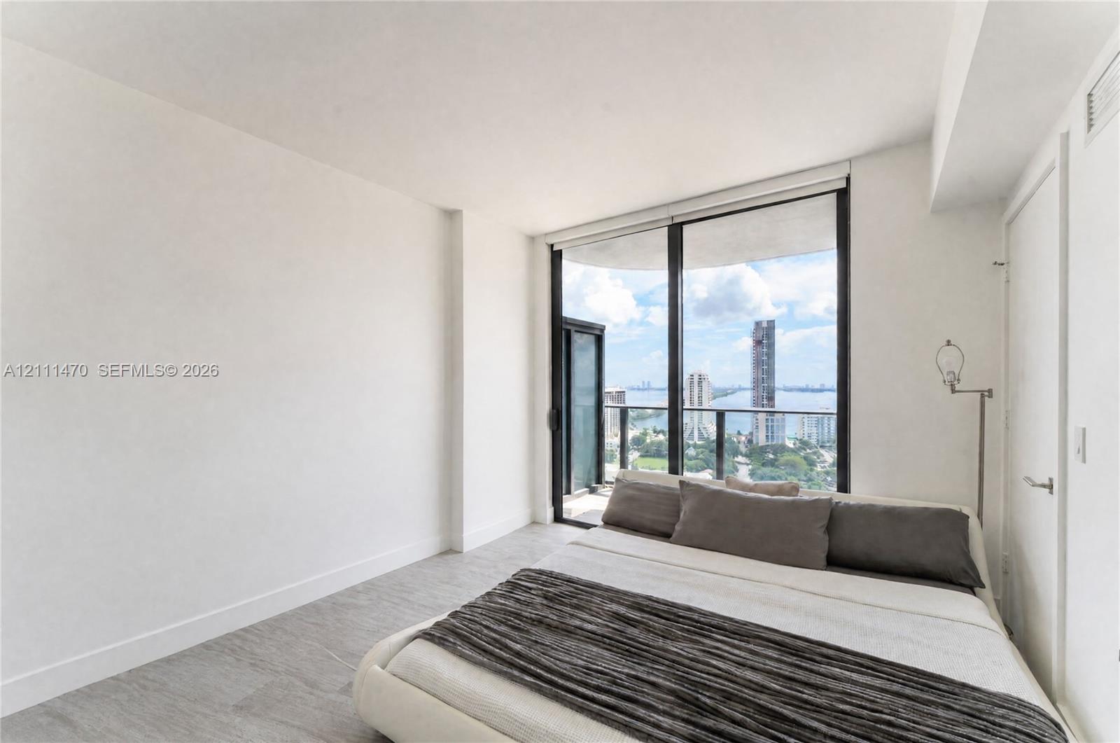 Floor-to-ceiling windows, private balcony access, neutral wall finishes, and wood-finish flooring