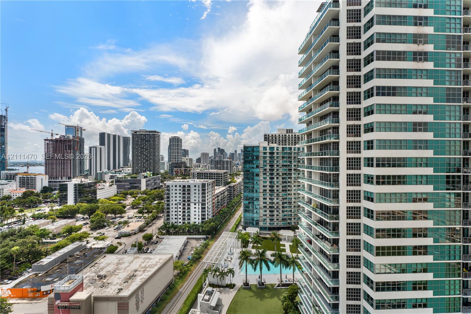High-rise building exterior featuring glass paneling, floor-to-ceiling windows, and private balconies, complemented by a ground-level swimming pool and manicured green space