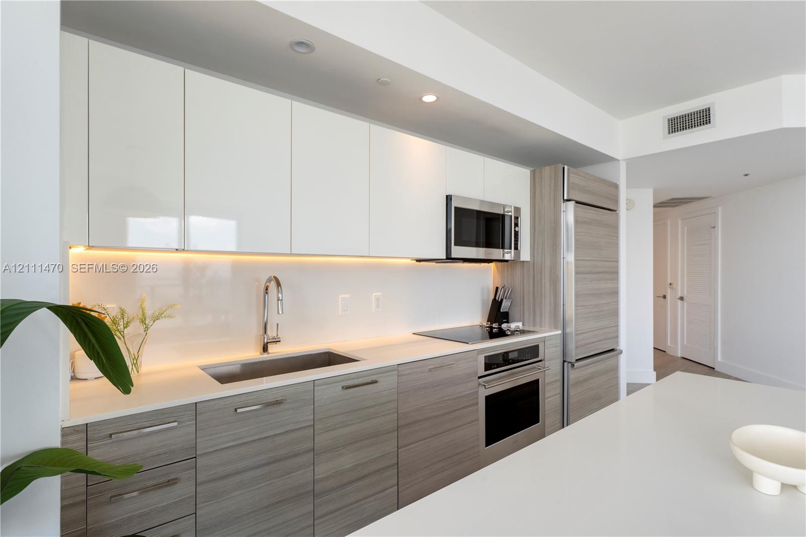 Kitchen featuring two-tone cabinetry, stone-surface countertops, integrated stainless steel refrigerator, built-in wall oven with matching cooktop, and under-cabinet task lighting