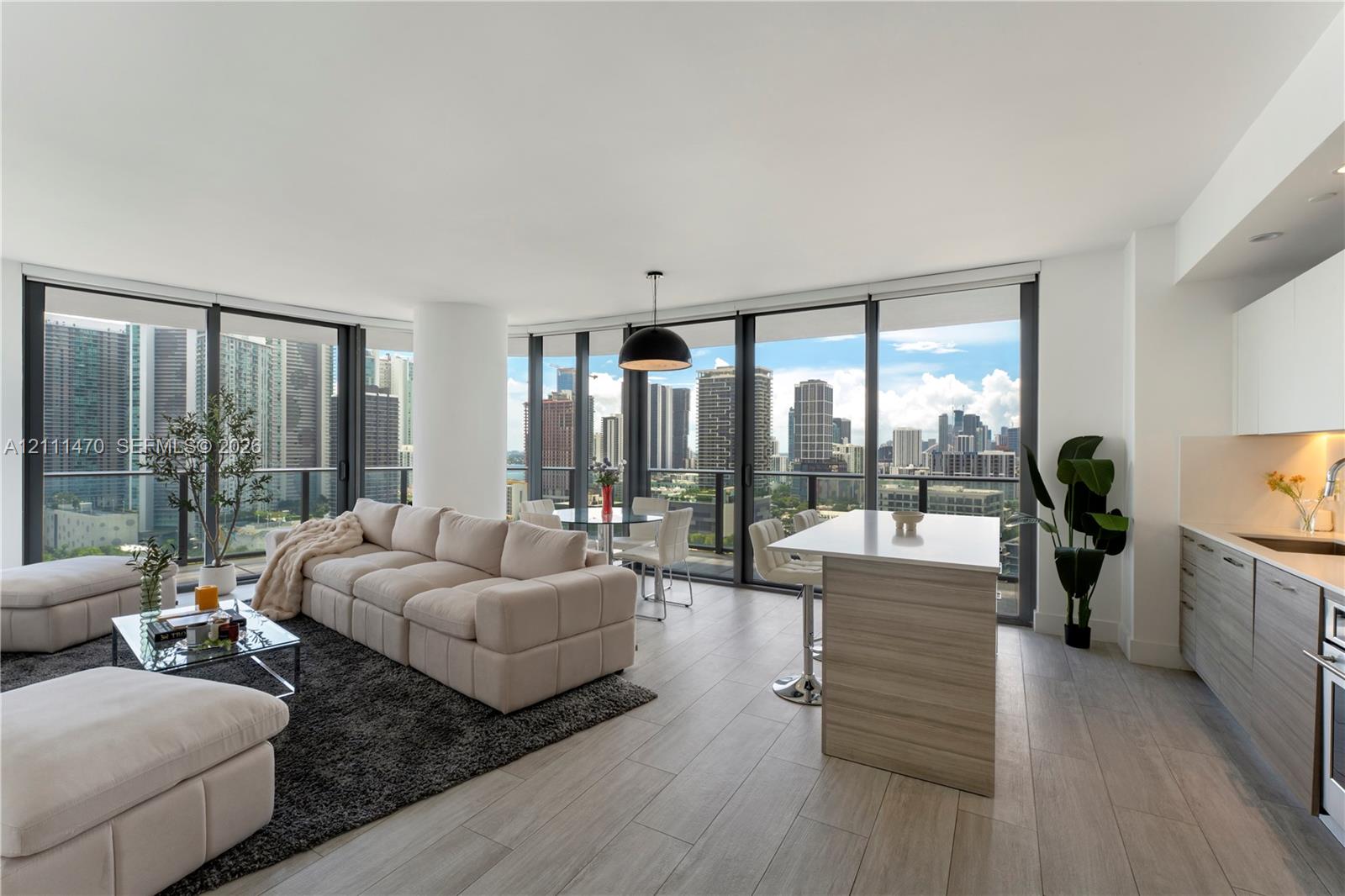 Open-concept living space featuring floor-to-ceiling windows, wood-finish flooring, a kitchen island with stone countertop, and contemporary pendant lighting