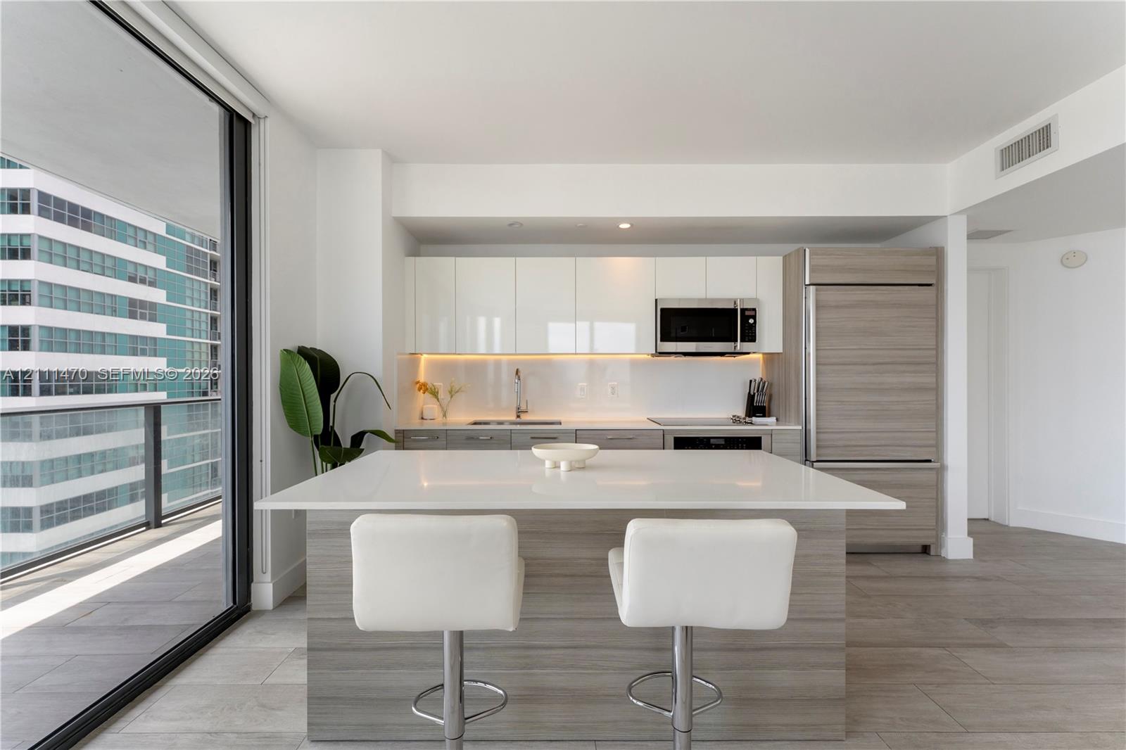 Kitchen featuring a white quartz island, high-gloss flat-panel cabinetry, integrated refrigerator, wood-finish lower cabinetry, and floor-to-ceiling glass sliding doors