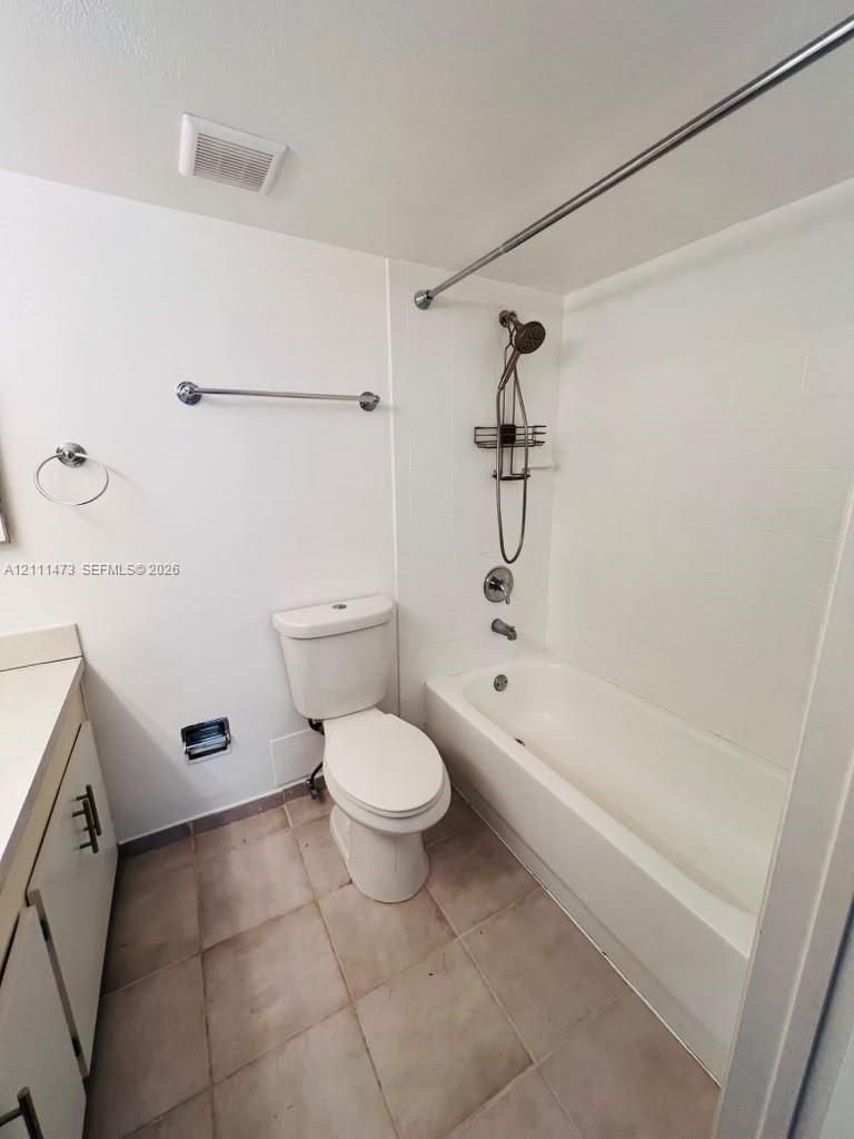 Bathroom featuring a shower-tub combination, a handheld showerhead, a neutral-toned tile floor, and a vanity with modern cabinet hardware