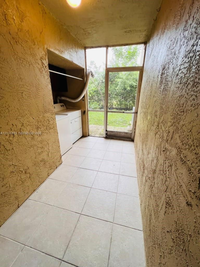 Enclosed utility area featuring textured walls, tile flooring, built-in recessed cabinetry, and a screened door leading to an outdoor space