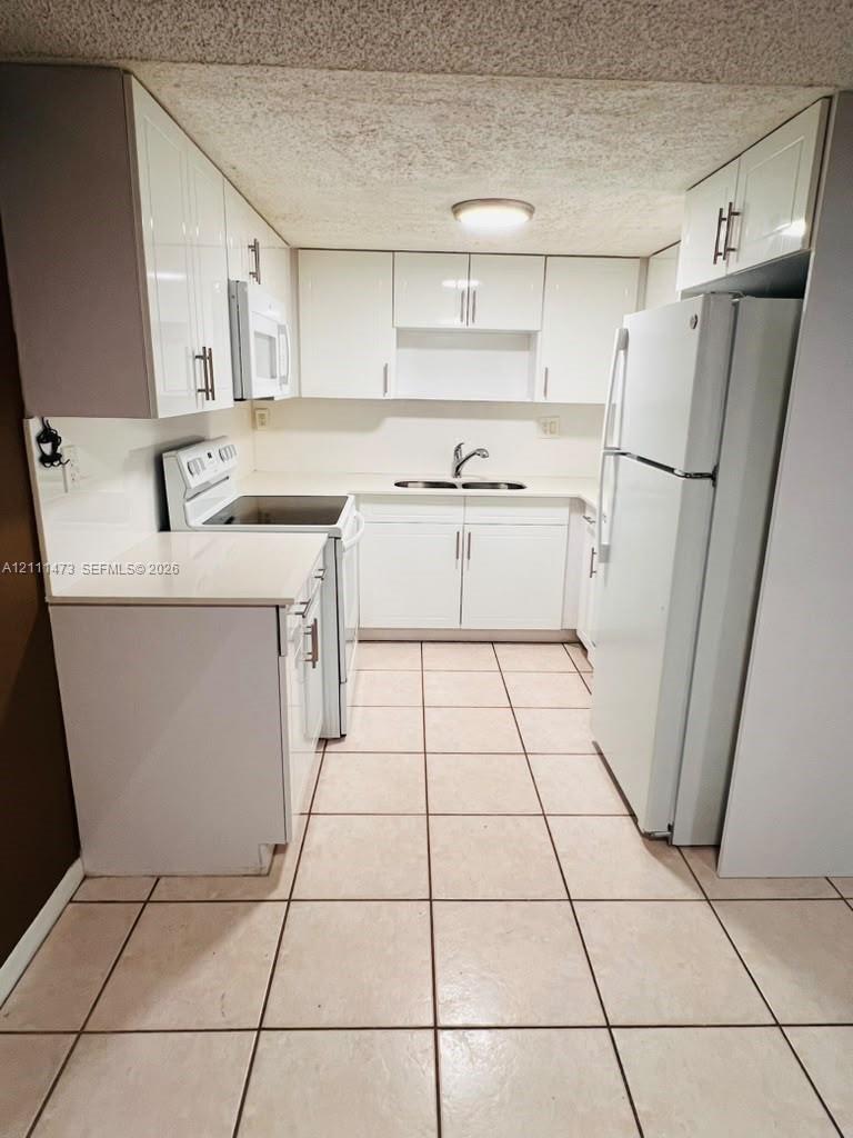 Kitchen featuring high-gloss white cabinetry, solid-surface countertops, dual-basin stainless steel sink with arch-neck faucet, and ceramic tile flooring Kitchen featuring high-gloss white cabinetry, solid-surface countertops, dual-basin stainless steel sink with arch-neck faucet, and ceramic tile flooring
