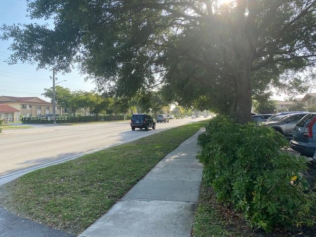 Concrete sidewalk bordered by mature shade trees, established shrubbery, and a grass lawn