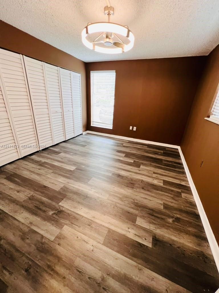 Room featuring wood-finish flooring, floor-to-ceiling louvered closet doors, and a contemporary circular flush-mount ceiling fixture with integrated lighting