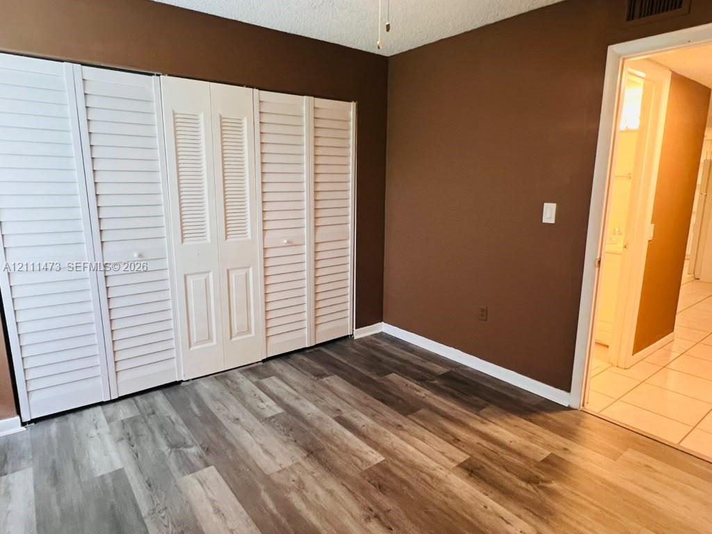 Room featuring wood-finish flooring and floor-to-ceiling white louvered-style closet doors Room featuring wood-finish flooring and floor-to-ceiling white louvered-style closet doors
