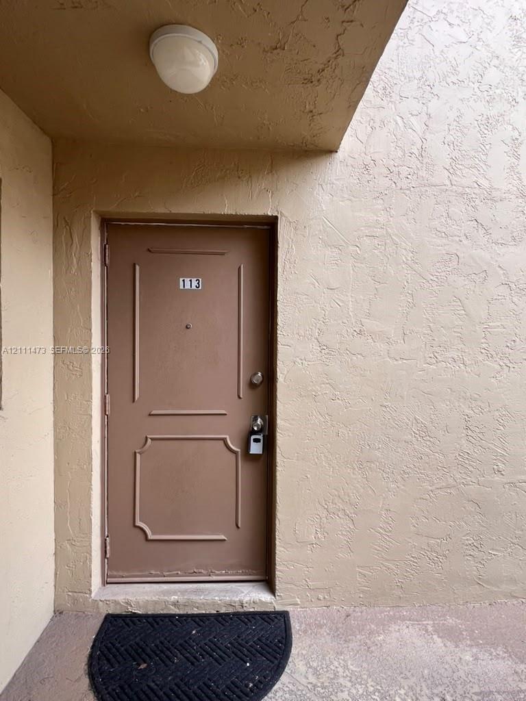 Exterior entrance featuring a solid-core door with decorative panel molding, a flush-mount overhead ceiling light, and textured stucco walls