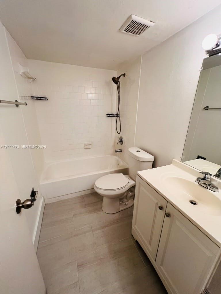 Bathroom featuring a tub-shower combination with white subway-style tile, vanity with an integrated basin, wood-finish tile flooring, and a wall-mounted hand-held shower fixture