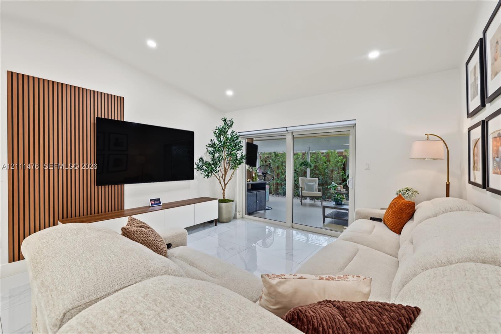 Living area featuring light-toned tile flooring, recessed lighting, and a decorative wood-slat accent wall