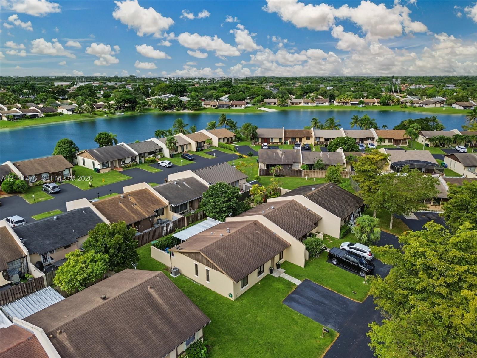 Aerial perspective of residential properties featuring shingle roofing, asphalt driveways, manicured green lawns, and proximity to a community lake
