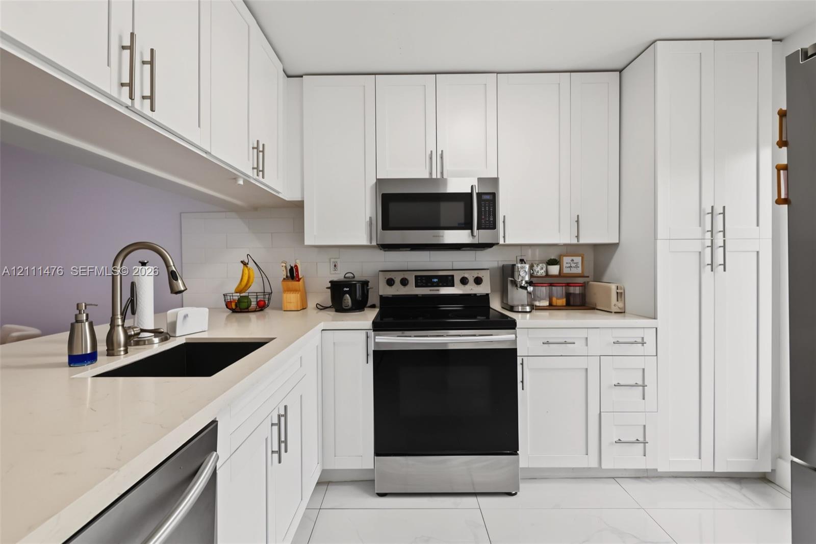 Kitchen featuring white shaker-style cabinetry, light-toned stone-surface countertops, subway tile backsplash, stainless steel appliances, and large-format tile flooring