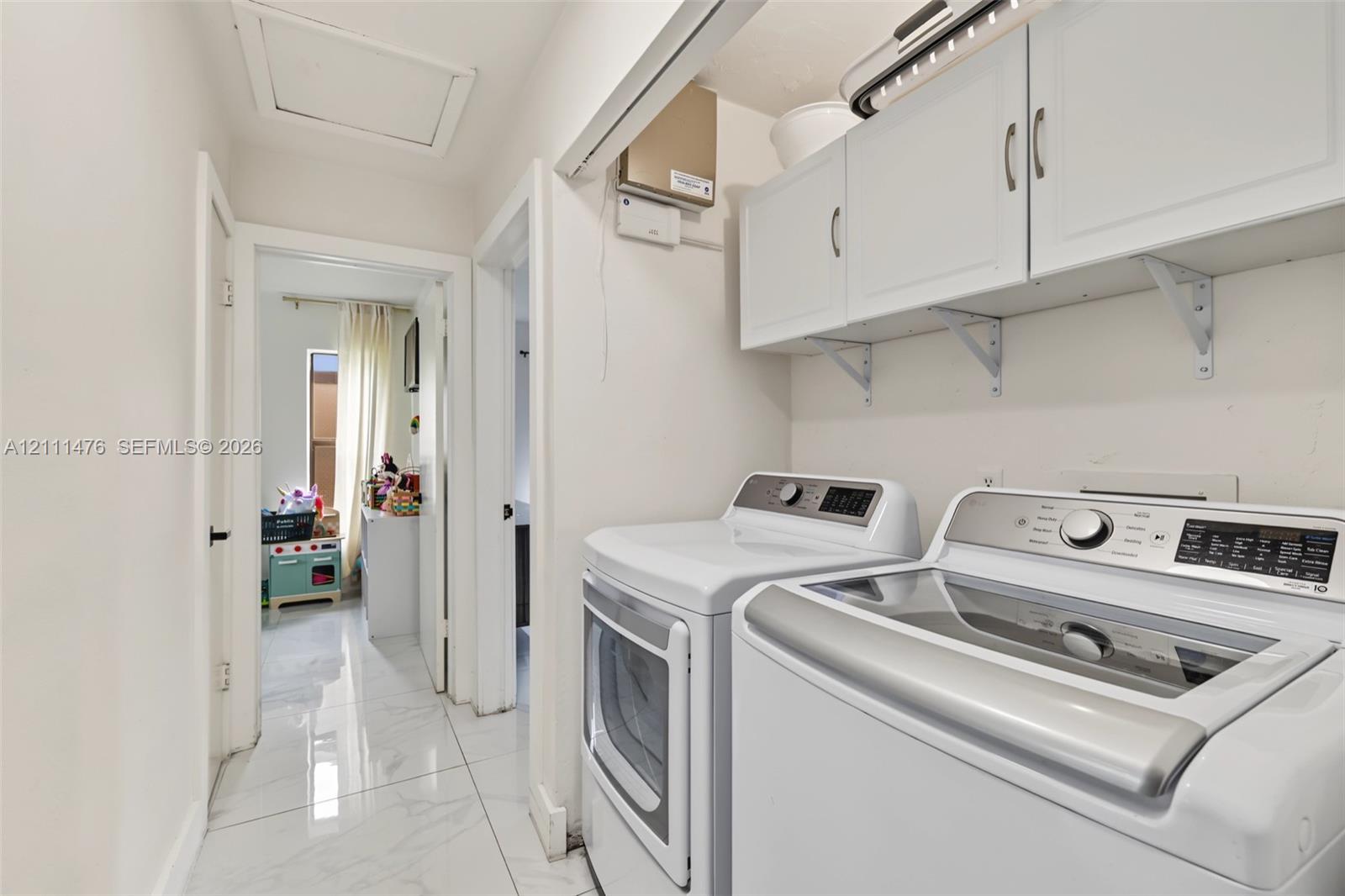Laundry area featuring white shaker-style wall-mounted cabinetry, polished stone-finish flooring, and recessed ceiling lighting