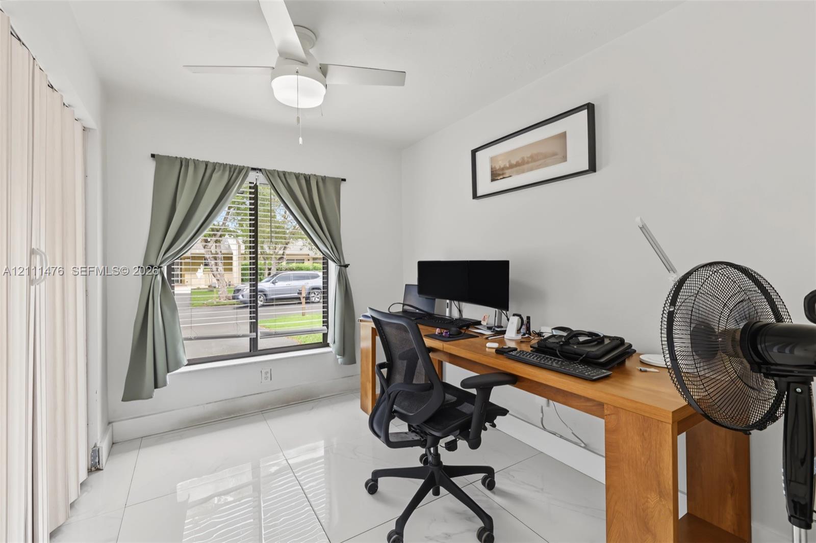 Neutral-toned interior space featuring polished tile flooring, a white ceiling fan with integrated lighting, and a single-pane window with horizontal blinds