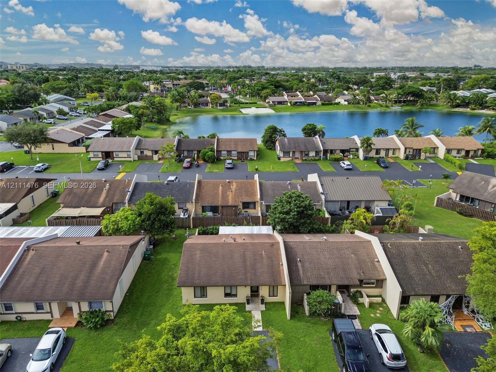 Aerial perspective featuring multi-unit residential structures, paved driveways, green space, and a waterfront backdrop