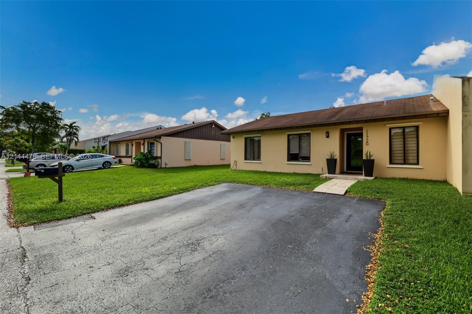 Single-story residence featuring a stucco exterior, asphalt shingle roof, paved driveway, and front lawn