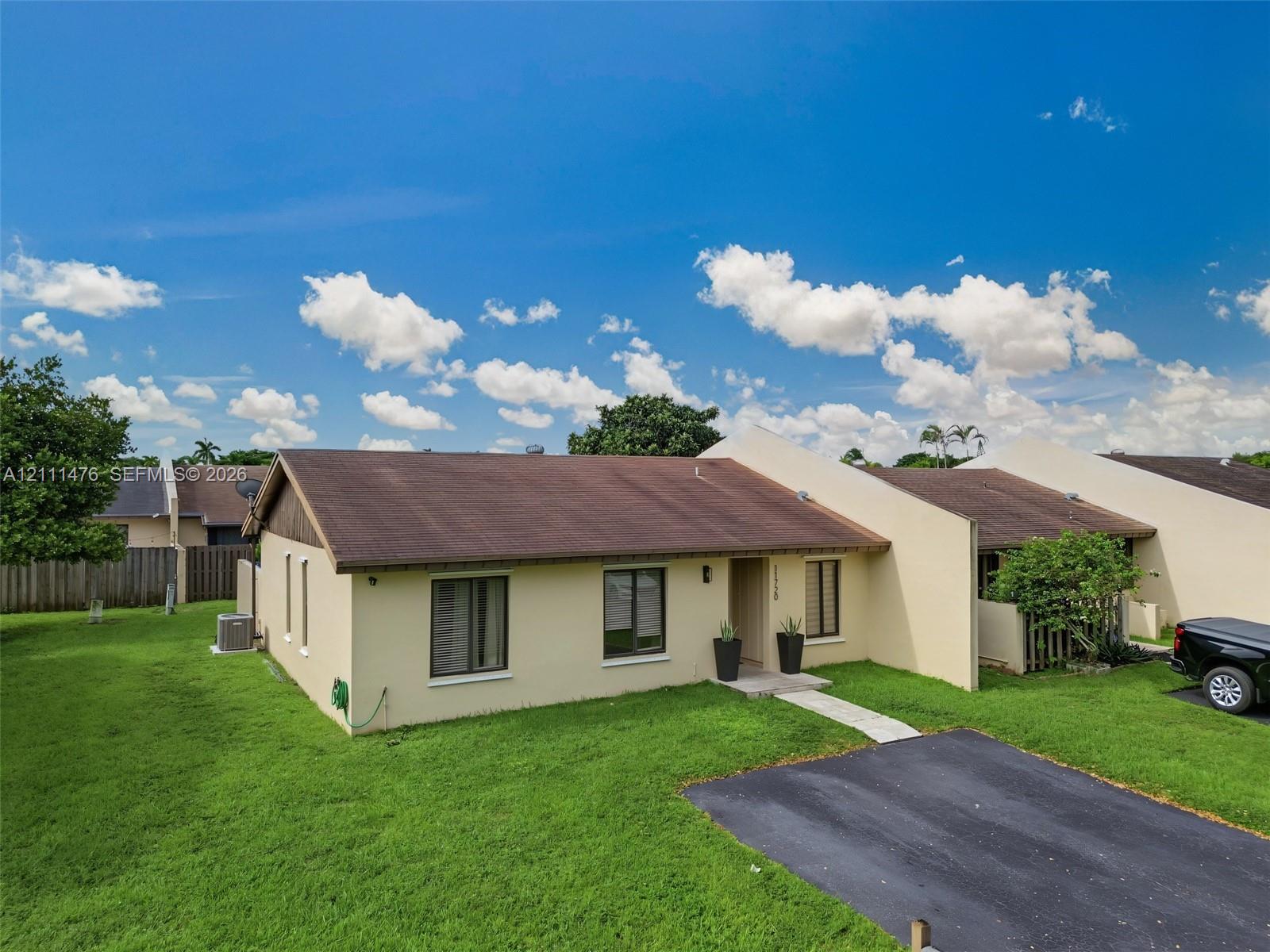Single-story exterior featuring light-toned stucco siding, a gabled roof, and a private asphalt driveway Single-story exterior featuring light-toned stucco siding, a gabled roof, and a private asphalt driveway