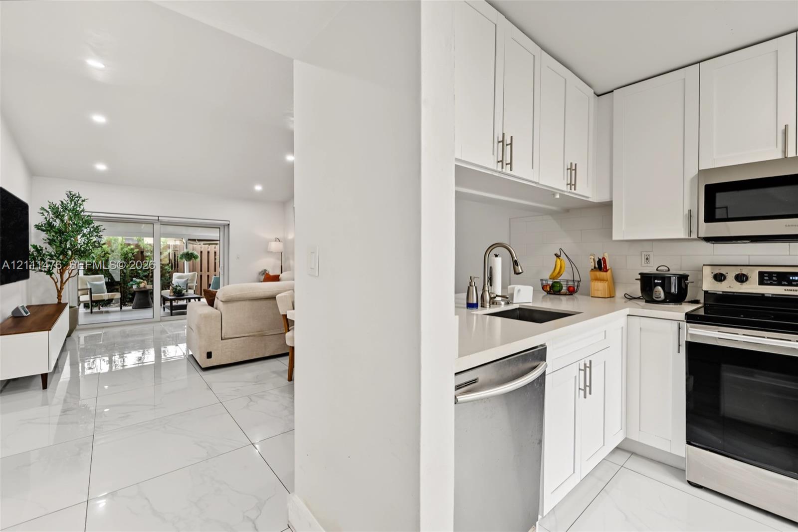 Kitchen featuring white cabinetry, solid-surface countertops, subway tile backsplash, and stainless steel appliances, complemented by polished tile flooring throughout