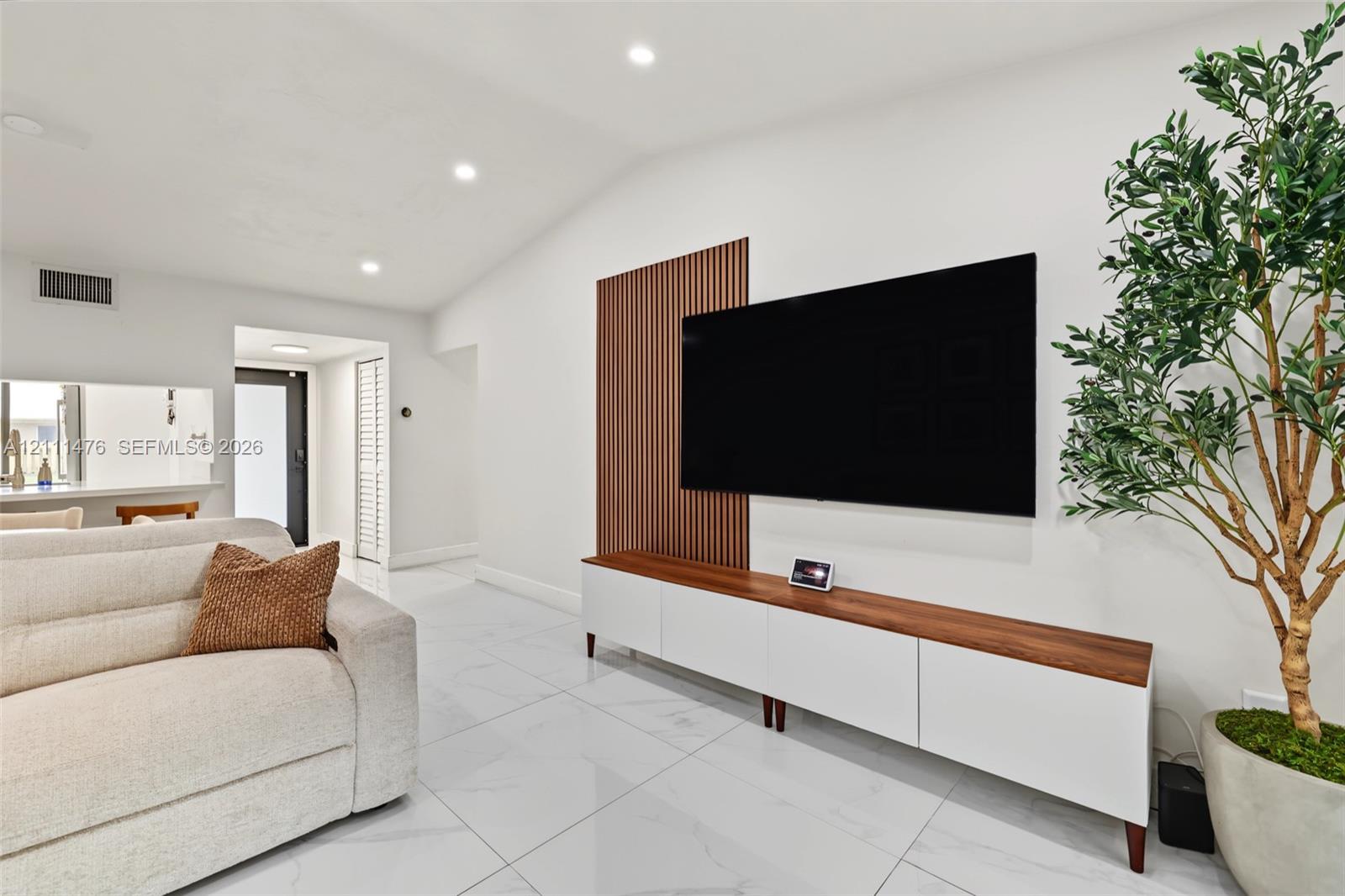 Vaulted ceilings, large-format tile flooring, recessed lighting, and a custom wood-slat accent wall with built-in cabinetry