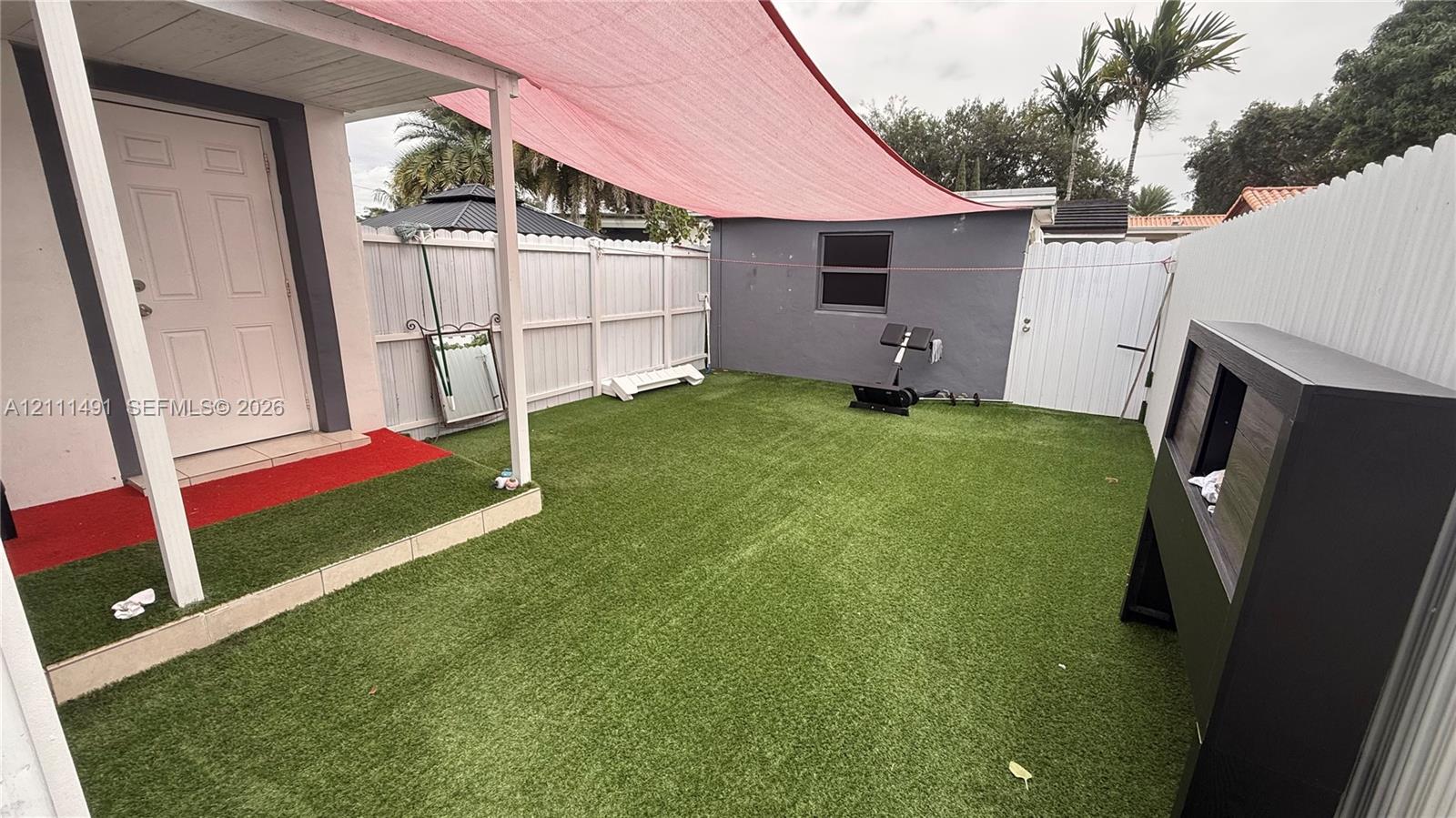 Fenced-in backyard featuring synthetic turf, a covered patio area, and overhead fabric sun shading