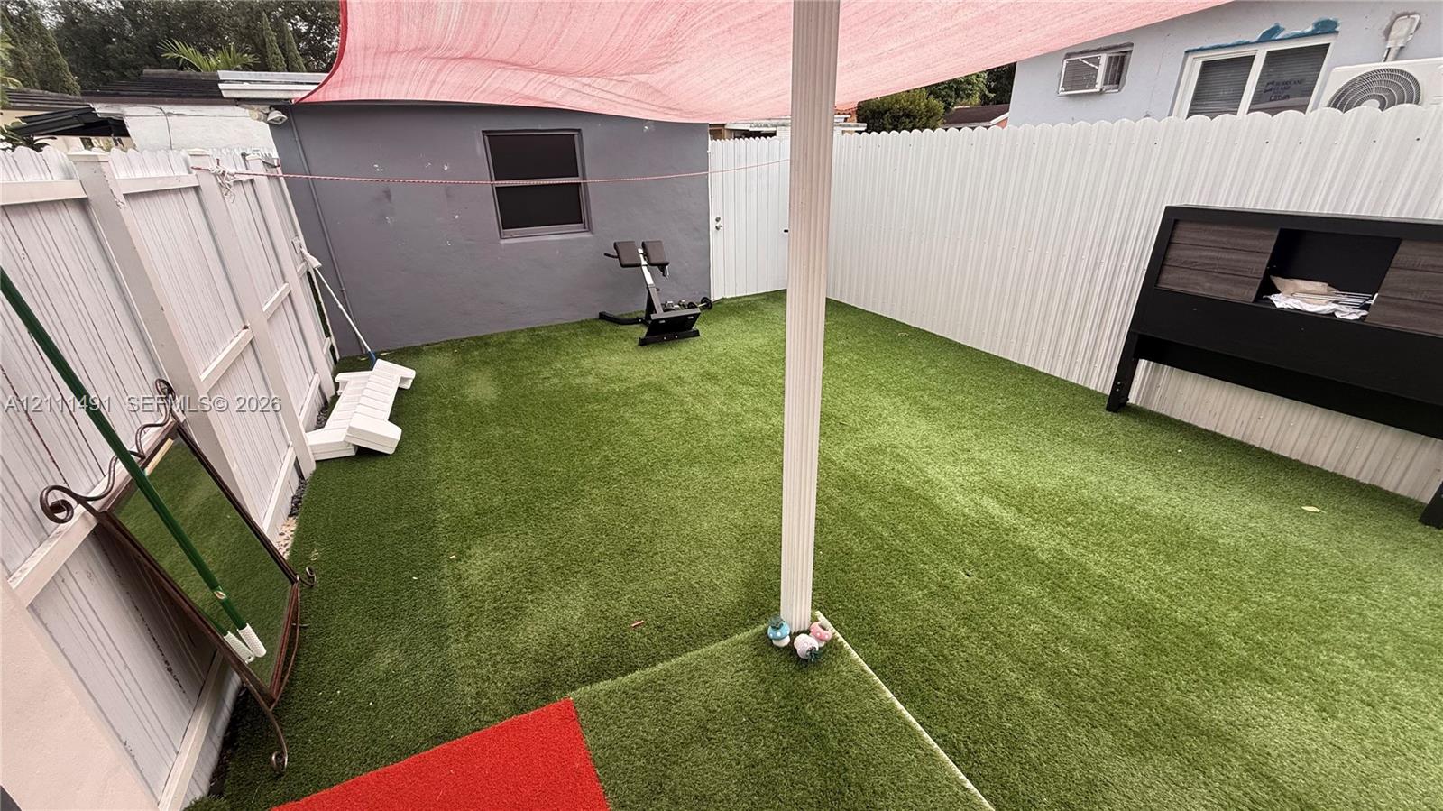 Enclosed backyard featuring synthetic turf, white vinyl privacy fencing, and a built-in overhead shade canopy