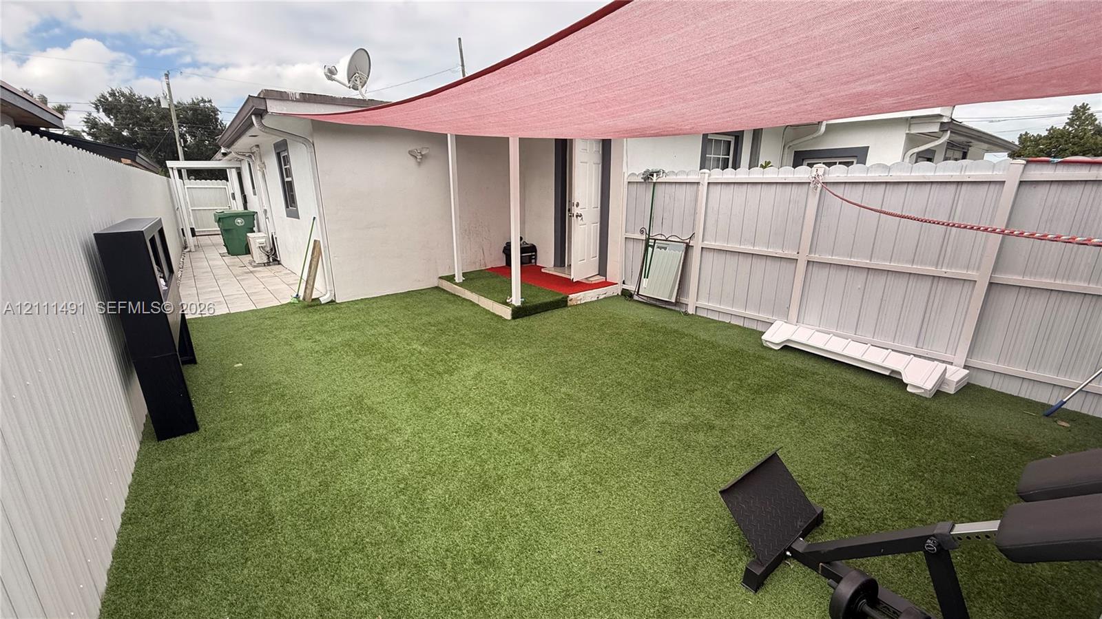 Fenced backyard featuring synthetic turf, a covered patio area, and white vinyl privacy fencing