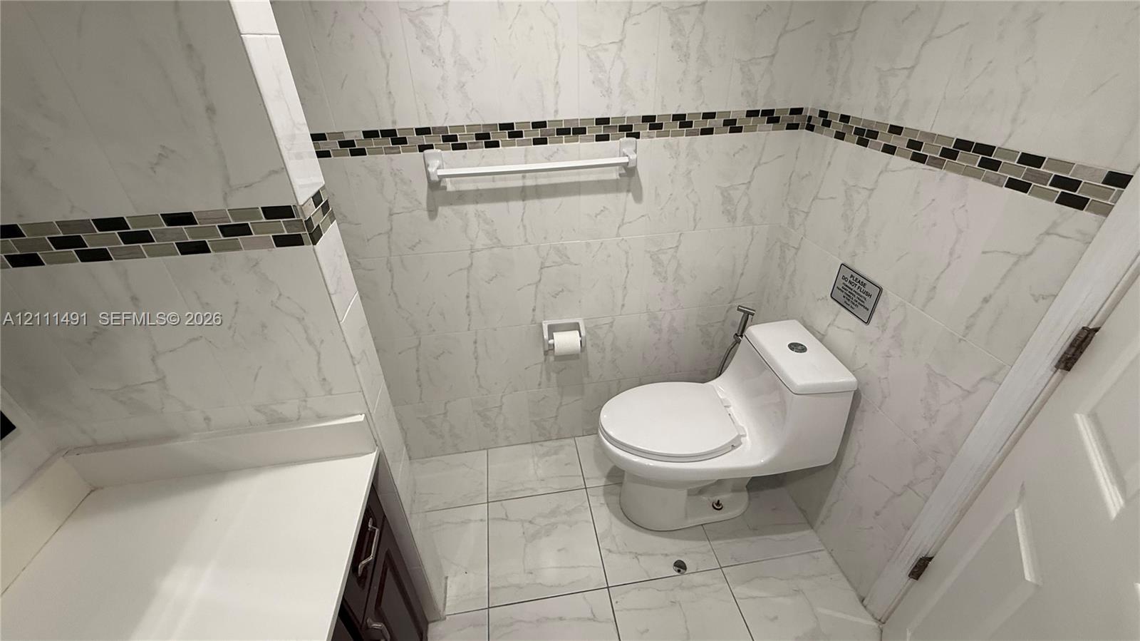 Bathroom featuring full-height wall tiling, integrated mosaic accent banding, large-format porcelain floor tile, and a one-piece toilet