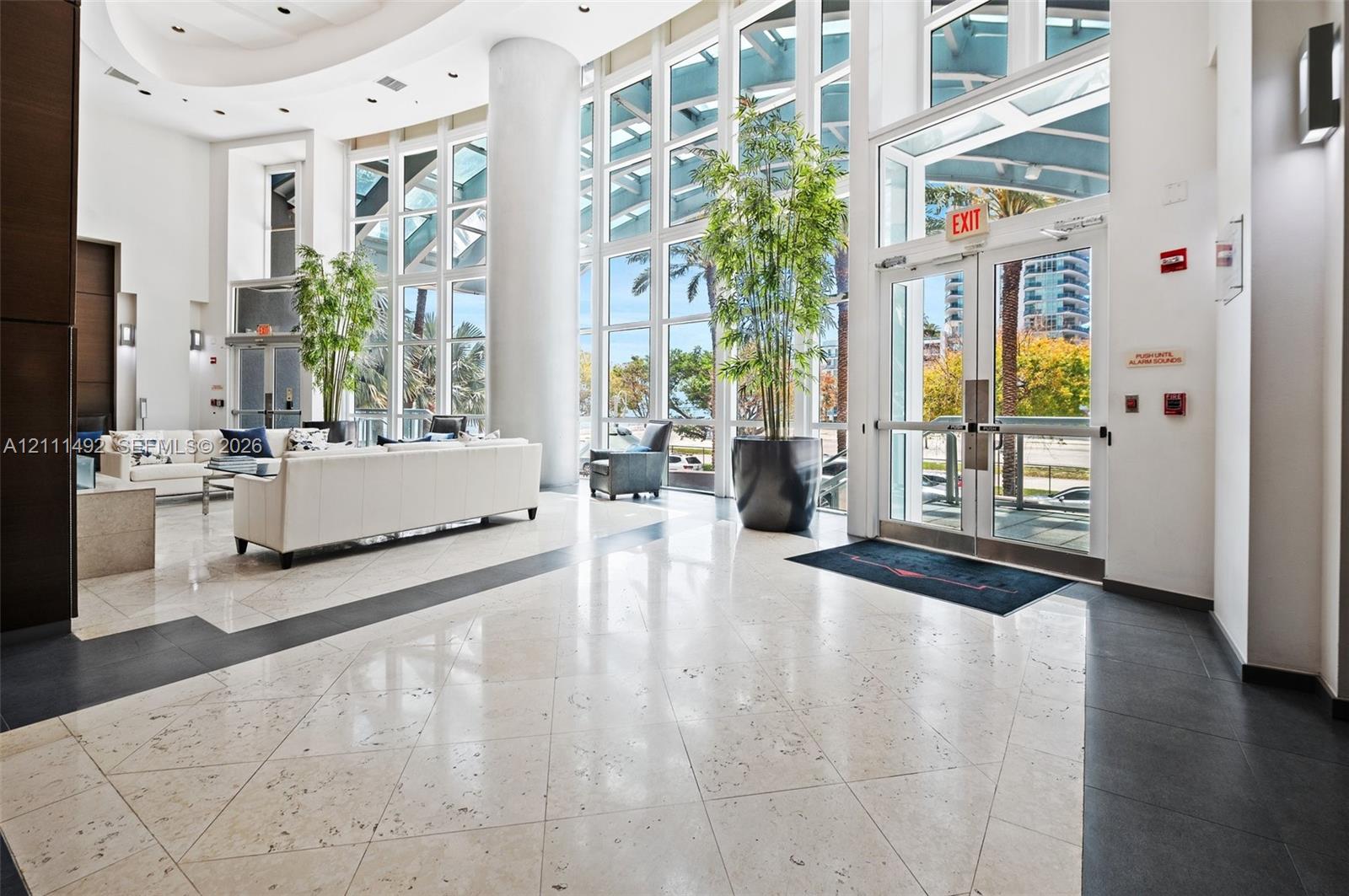 Grand lobby entrance featuring two-story floor-to-ceiling windows, polished stone tile flooring with decorative inlay, and a circular recessed ceiling design