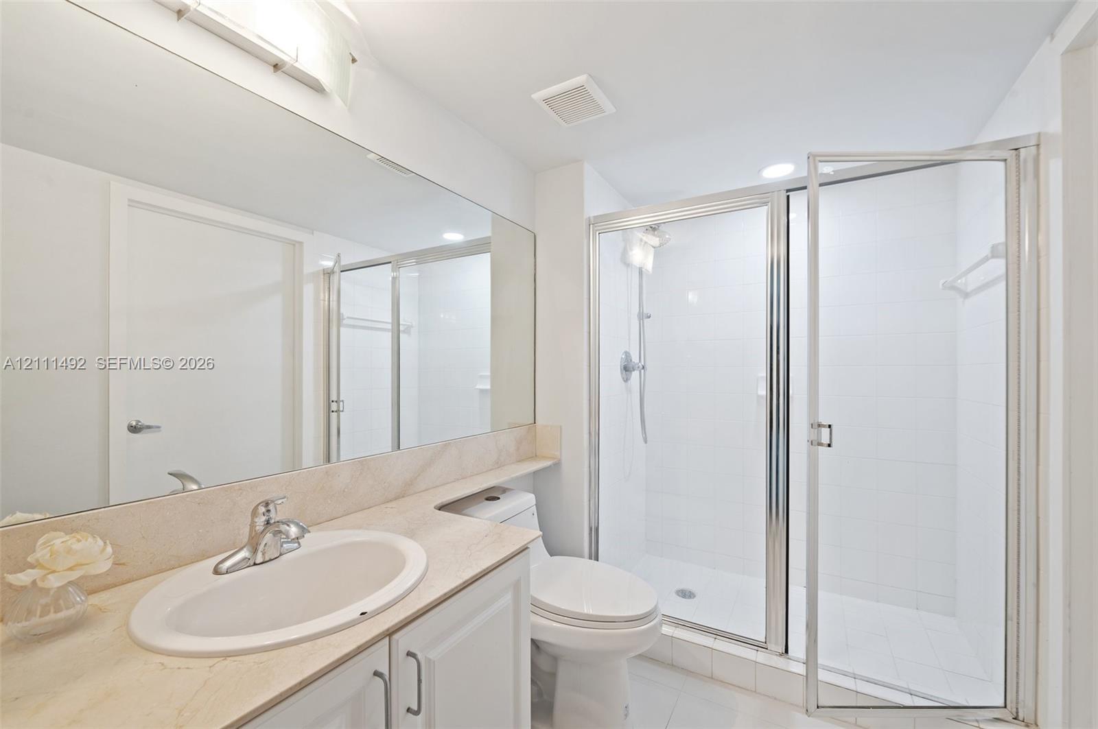 Bathroom featuring an integrated vanity with a stone-finish countertop, full-width vanity mirror, polished chrome faucet, and a walk-in shower with a glass enclosure