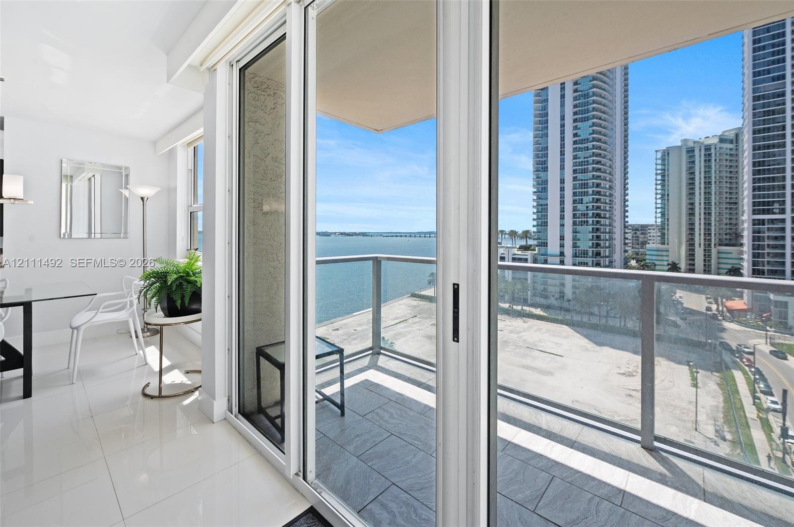 Private balcony featuring grey tile flooring and a glass-panel railing, floor-to-ceiling sliding glass doors, and polished white tile flooring