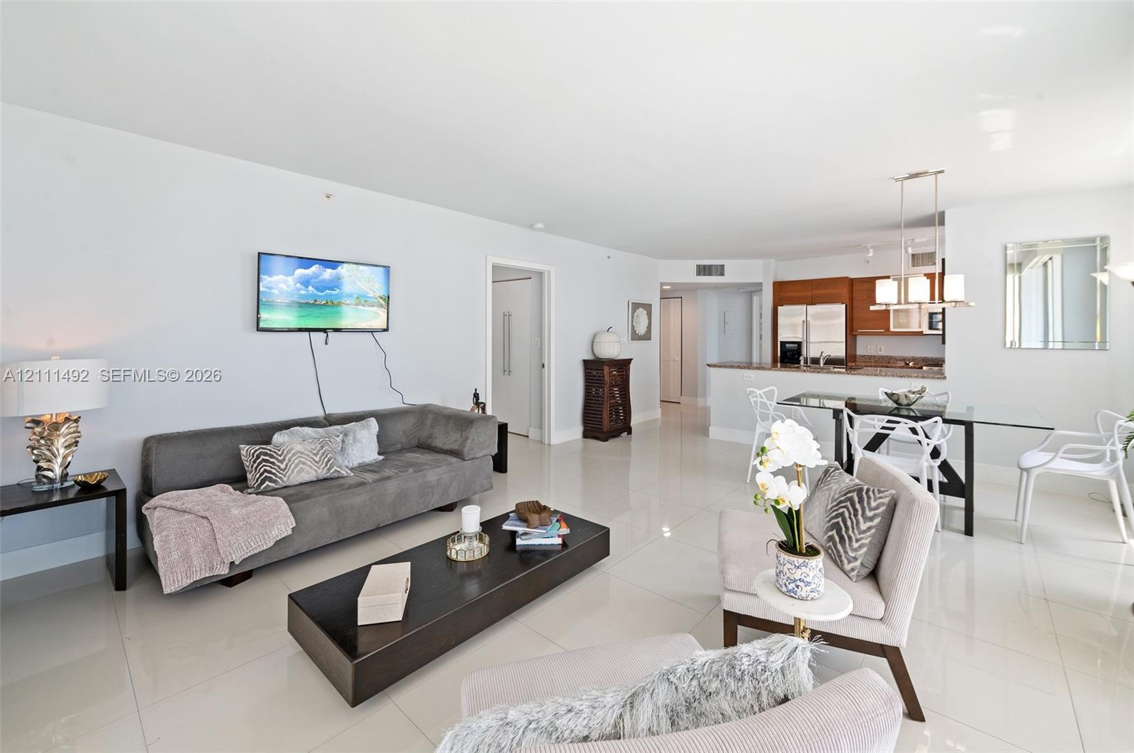 Open-concept living space featuring high-gloss tile flooring, recessed ceiling lighting, and a kitchen equipped with natural wood-finish cabinetry and stone countertops