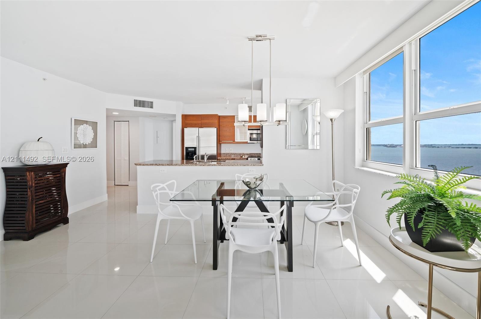 Open-concept kitchen and dining area featuring glossy tile flooring, wood-finish cabinetry, stone countertops, and floor-to-ceiling windows with water scenery