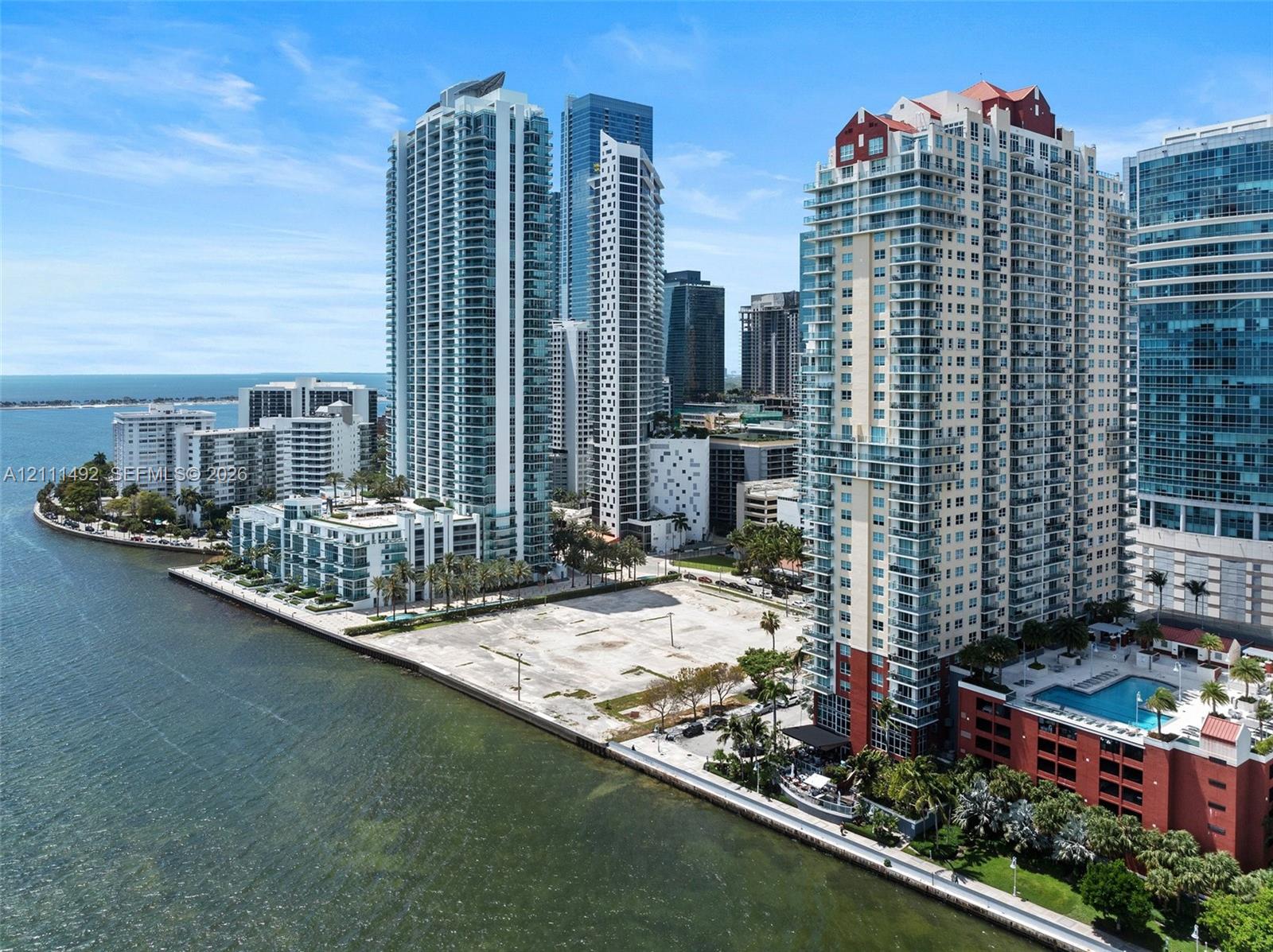 Aerial perspective of a waterfront high-rise featuring an outdoor swimming pool, direct shoreline access, and proximity to an urban skyline