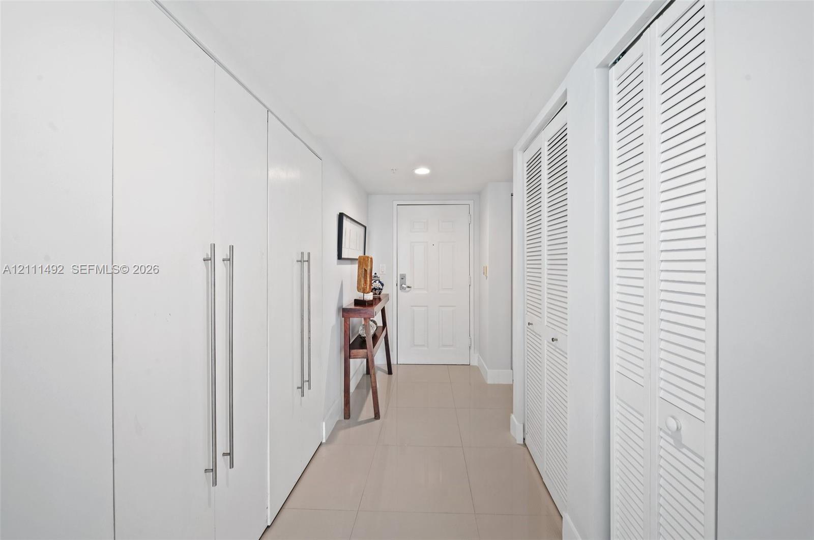 Entryway featuring large-format tile flooring, built-in floor-to-ceiling cabinetry with stainless steel bar pulls, and dual louvered closet doors