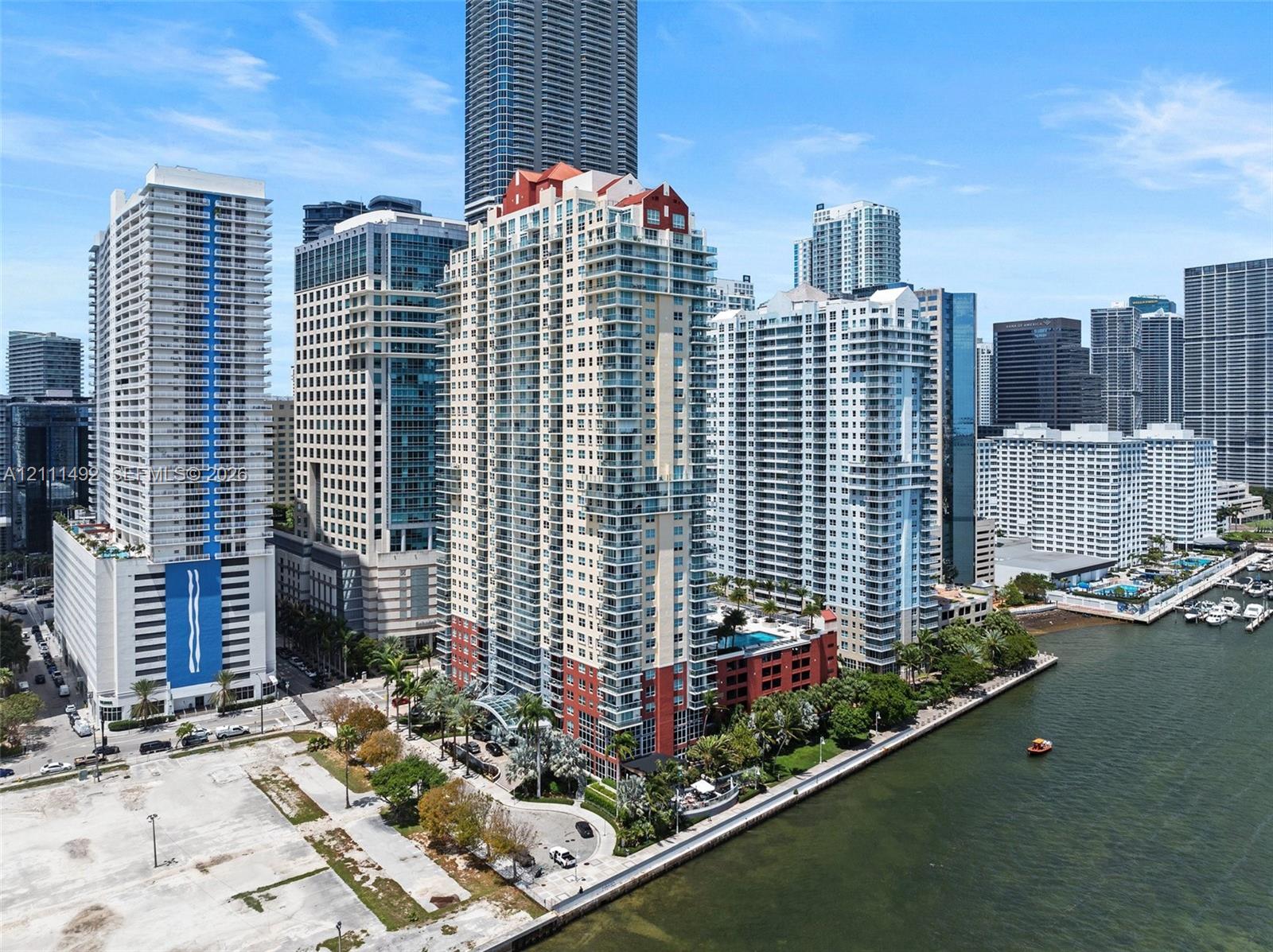 High-rise residential tower featuring a multi-story exterior, stacked glass balconies, a red-tiled roofline, and ground-level porte-cochre entry