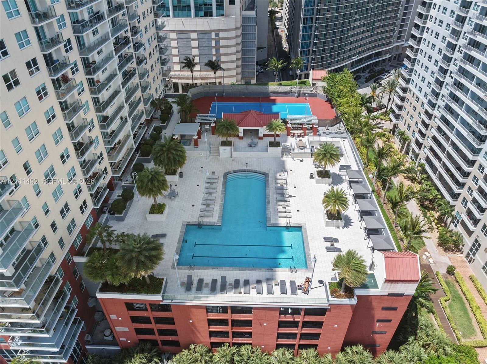 Elevated deck featuring a swimming pool, tennis court, tiled patio, palm tree landscaping, and a covered lounge area