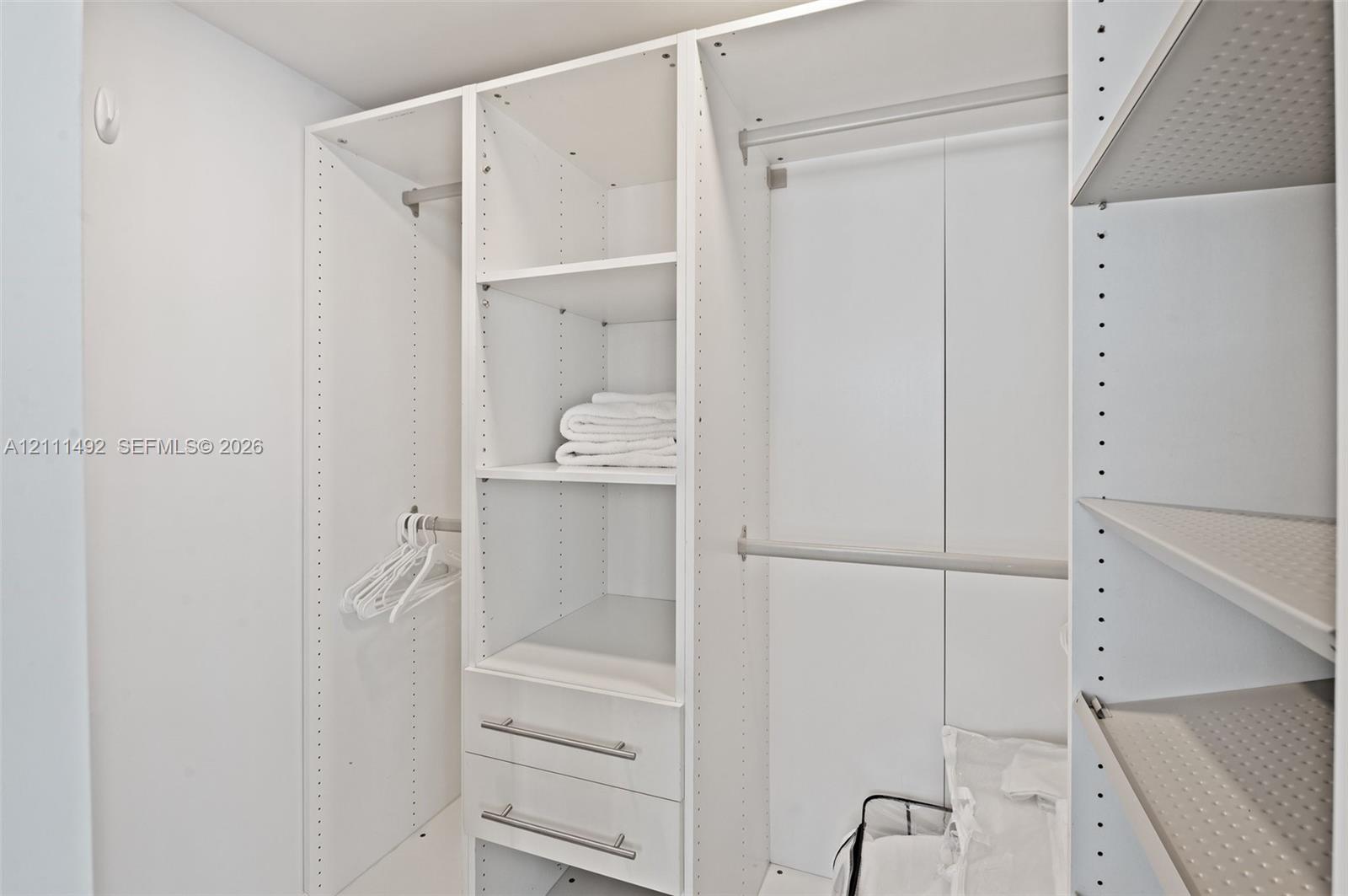 Custom walk-in closet featuring white modular built-in shelving, adjustable shelving units, integrated hanging rods, and two built-in storage drawers with metallic pulls