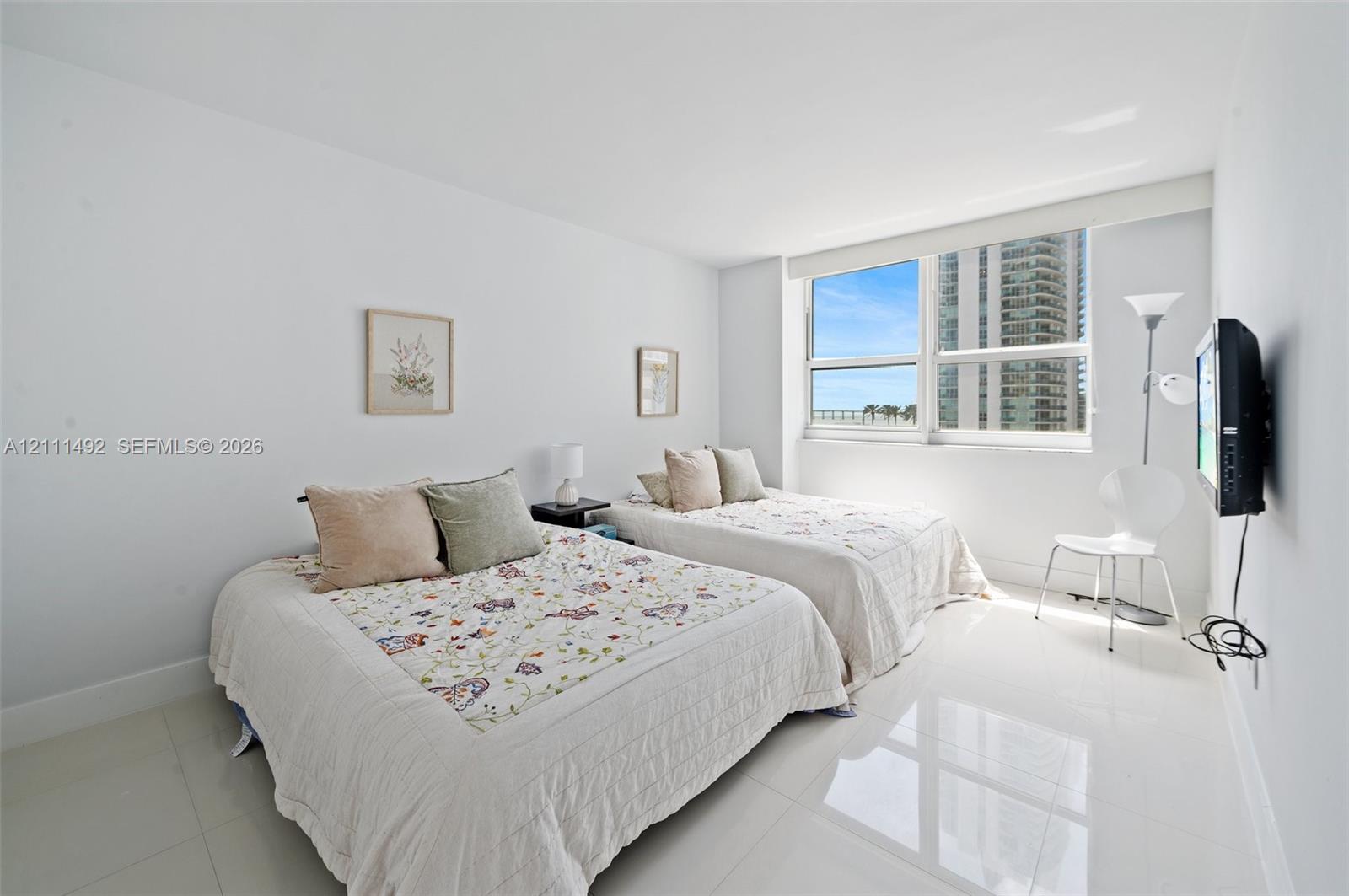 Neutral-toned interior space featuring polished tile flooring, crisp white walls, and a large horizontal window with a fitted roller shade