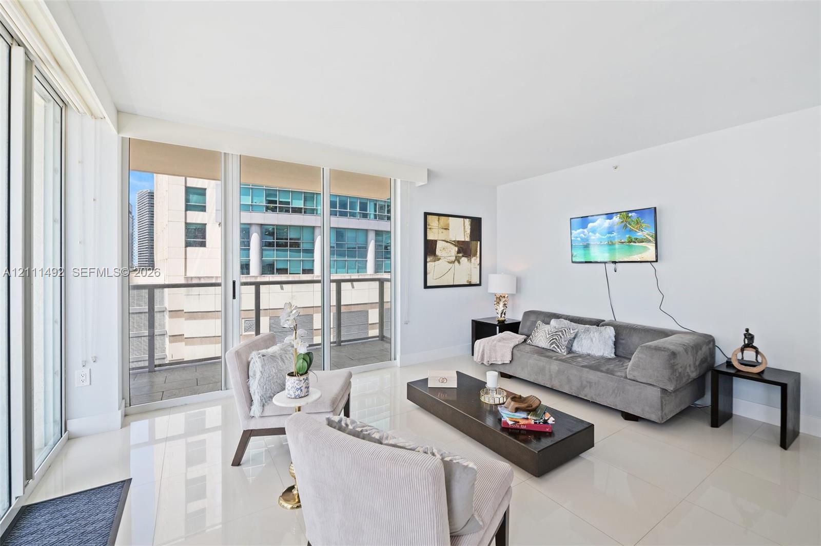 Floor-to-ceiling glass sliding doors, polished tile flooring, and a private balcony featuring metal railing