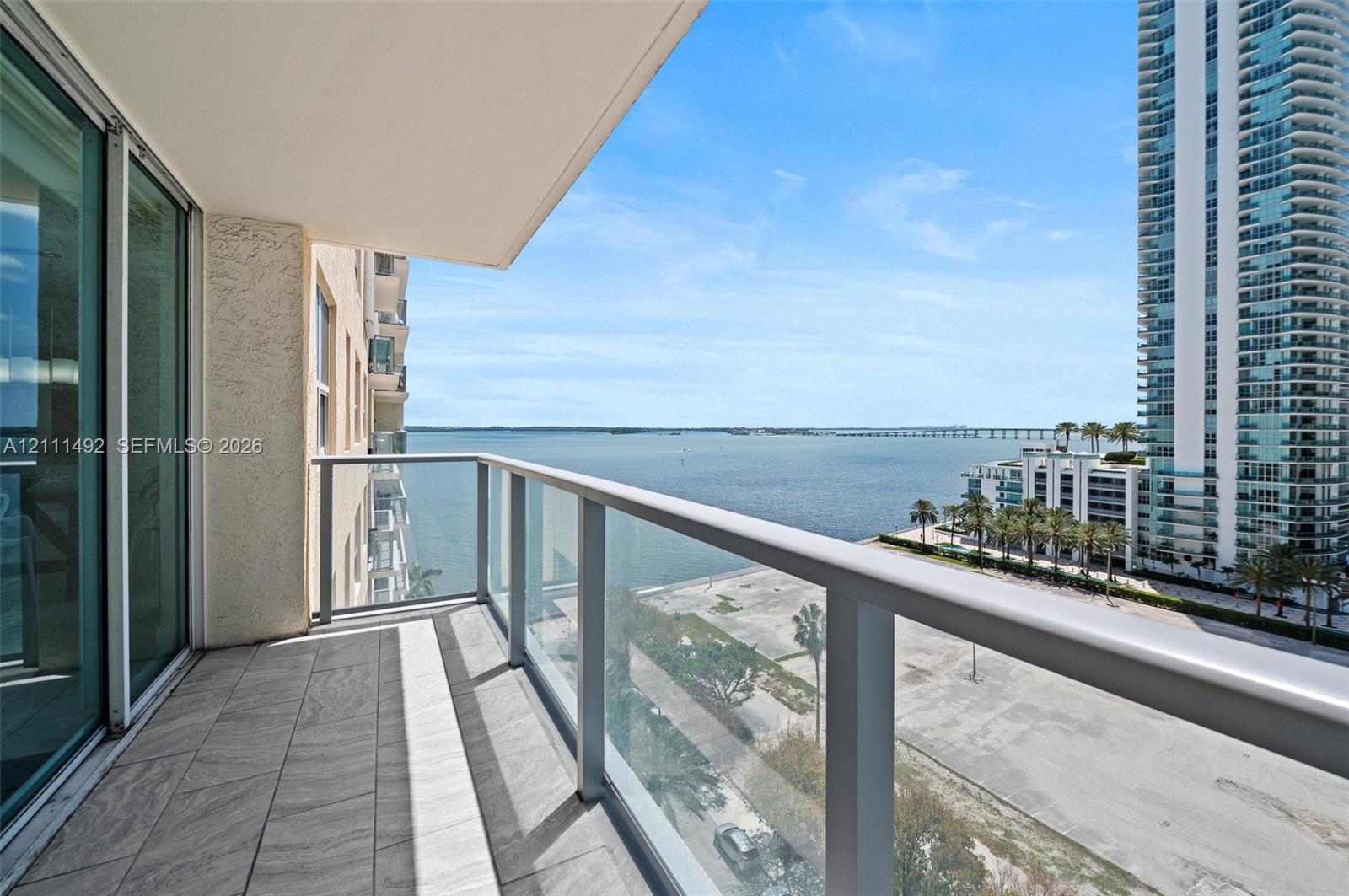 Private balcony featuring tiled flooring, glass panel railings, and expansive water and urban scenery