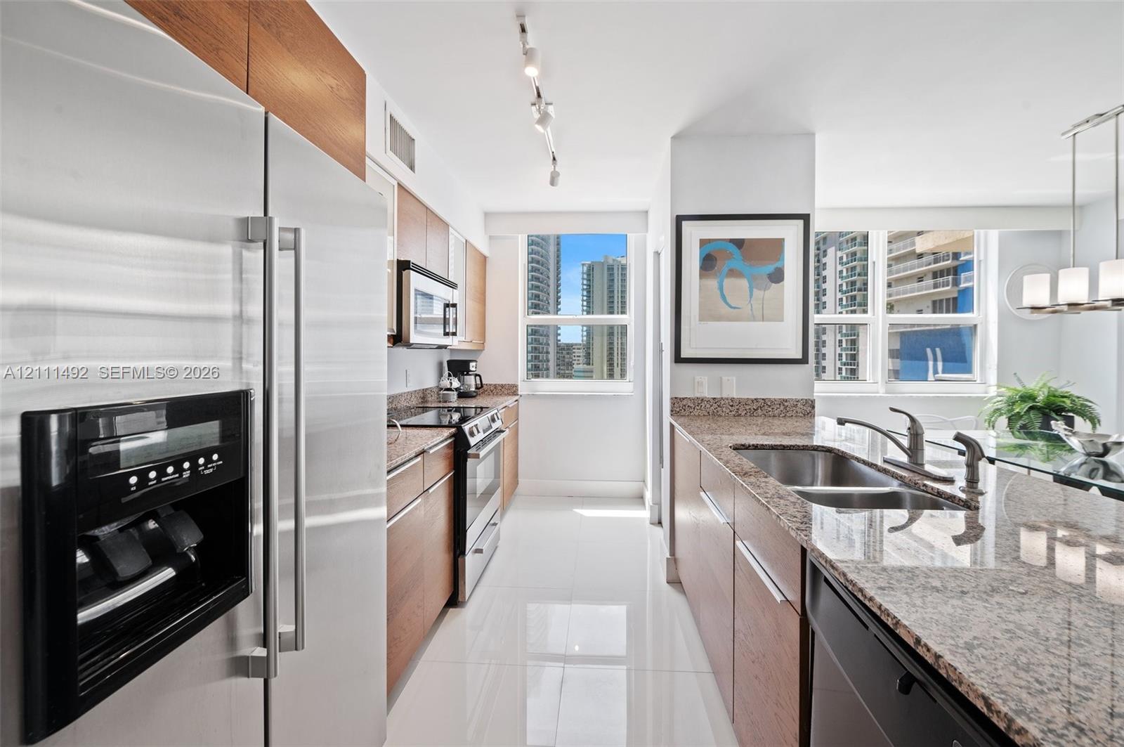 Kitchen featuring wood-finish cabinetry, stone countertops, stainless steel appliances, a double-basin sink, and tile flooring