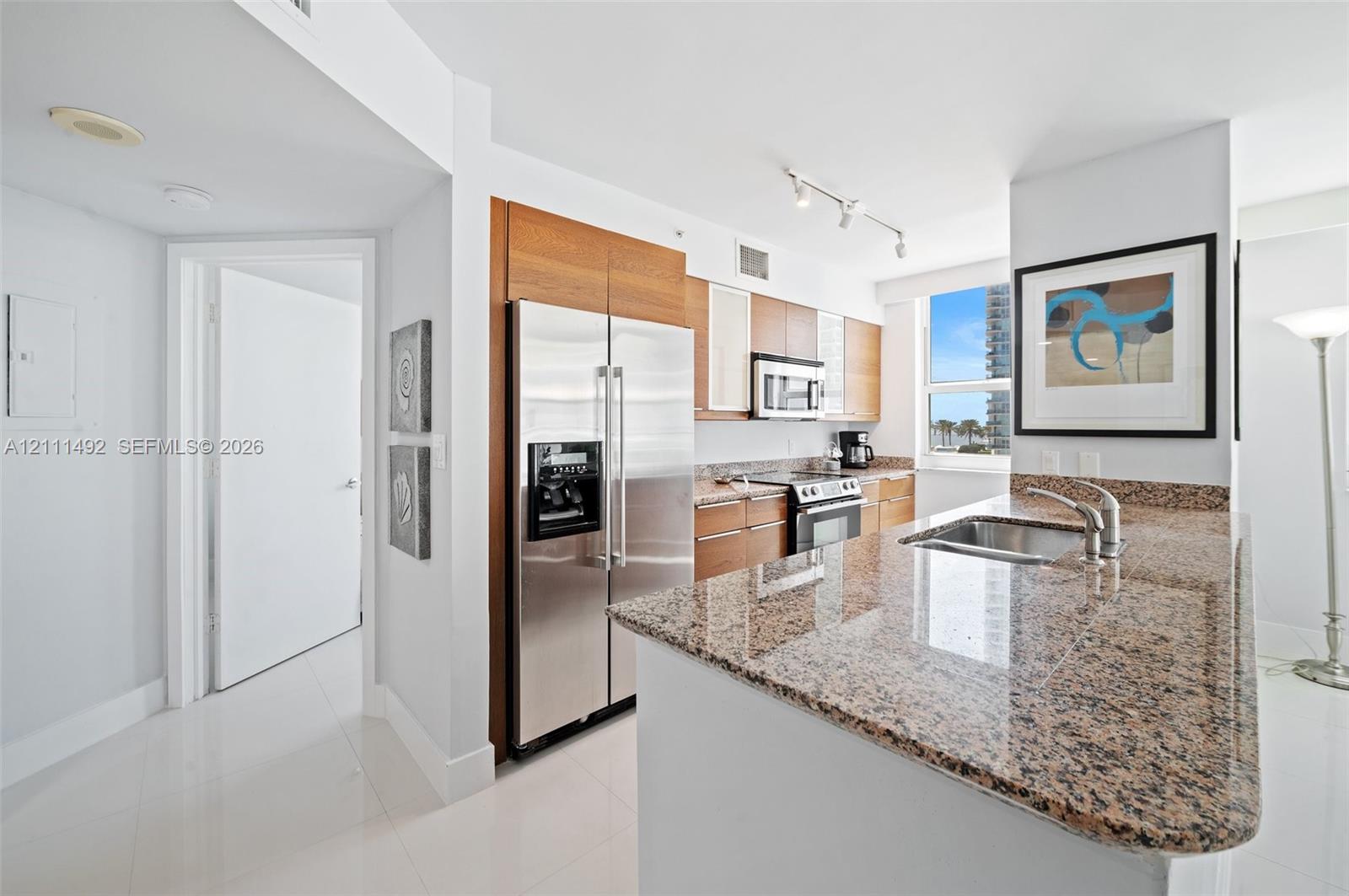 Kitchen featuring light wood-finish cabinetry, stone countertops, stainless steel appliances, and a breakfast bar with an integrated sink