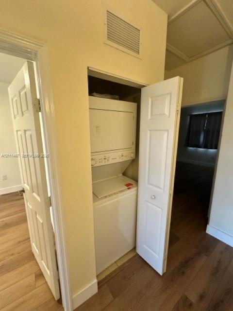Laundry closet featuring a stackable washer and dryer unit, wood-finish flooring, and panel-style interior doors