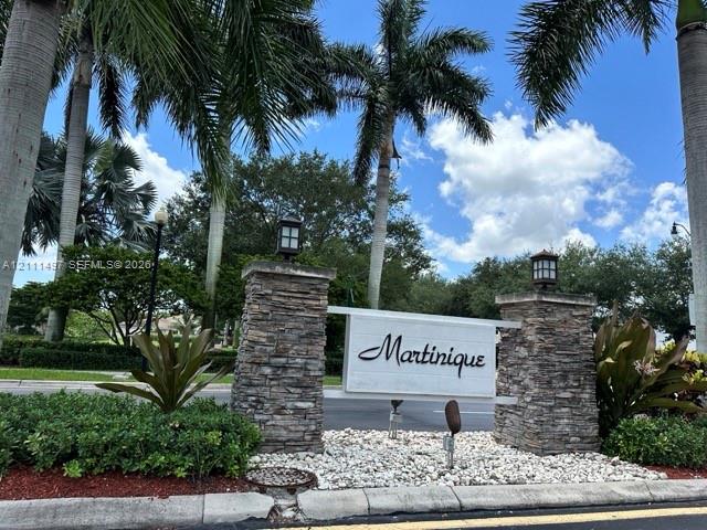 Community entrance featuring stacked-stone pillars, capped lantern-style lighting, and mature palm landscaping.
